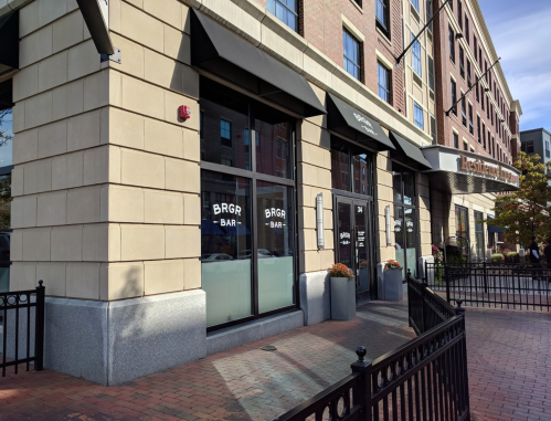 Exterior view of a restaurant with large windows, featuring a sign that reads "BRGR BAR" and a brick walkway.