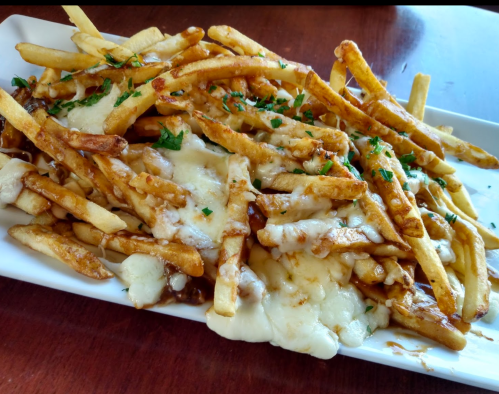 A plate of cheesy fries topped with melted cheese and garnished with parsley on a wooden table.