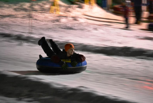 A person joyfully sledding down a snowy hill on a blue inner tube at night.