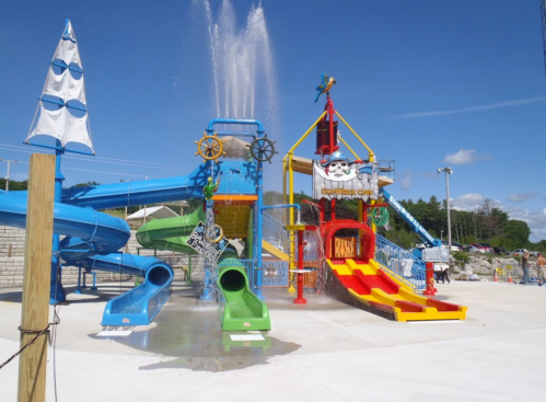 Colorful water slides and a splash pad at a water park under a clear blue sky.