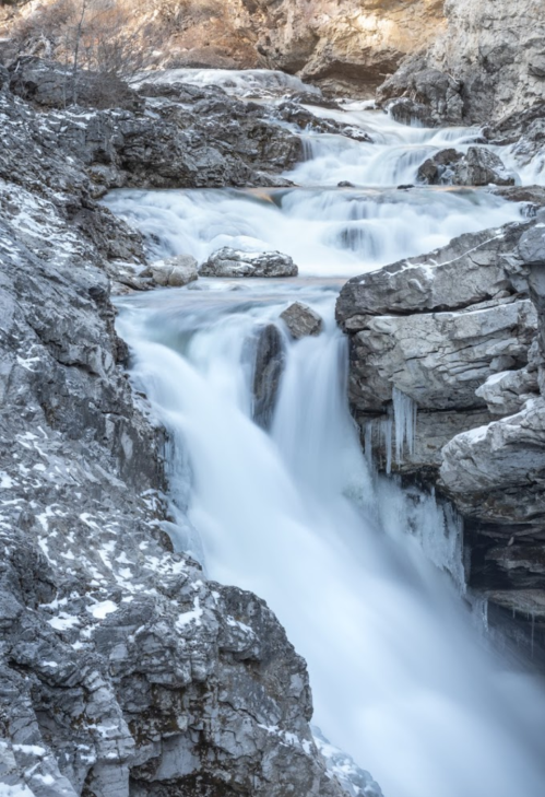 A serene waterfall cascades over rocky terrain, surrounded by icy formations and a winter landscape.