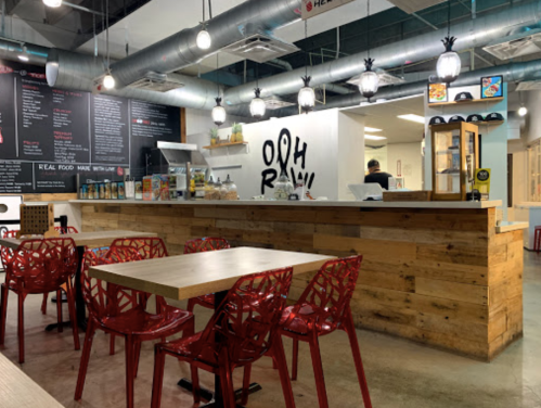 A modern restaurant interior featuring wooden counters, red chairs, and a menu board on the wall.