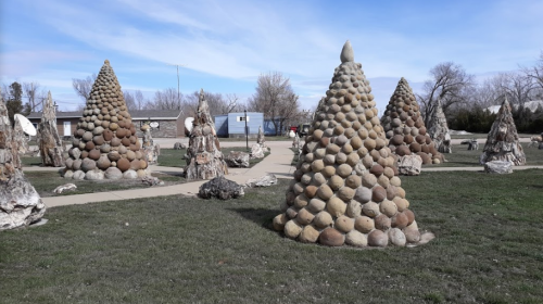 A landscape featuring several cone-shaped stone sculptures arranged along a pathway in a grassy area.