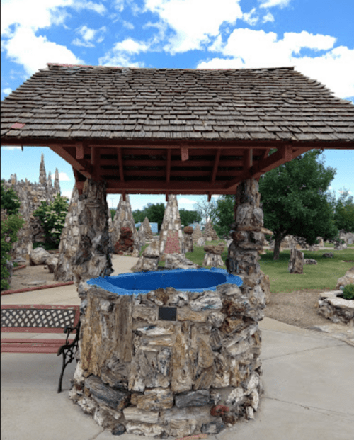 A stone well with a wooden roof and blue water, surrounded by unique rock formations and greenery under a blue sky.