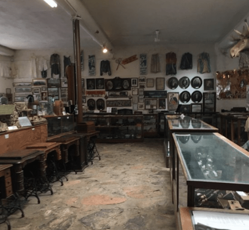 A vintage museum interior with glass display cases, wooden furniture, and walls adorned with various historical artifacts.