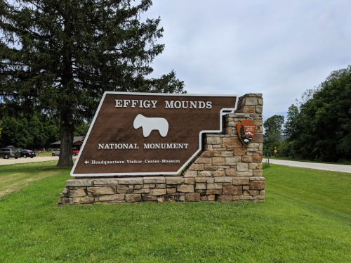 Sign for Effigy Mounds National Monument, featuring a stone base and information about the visitor center and museum.