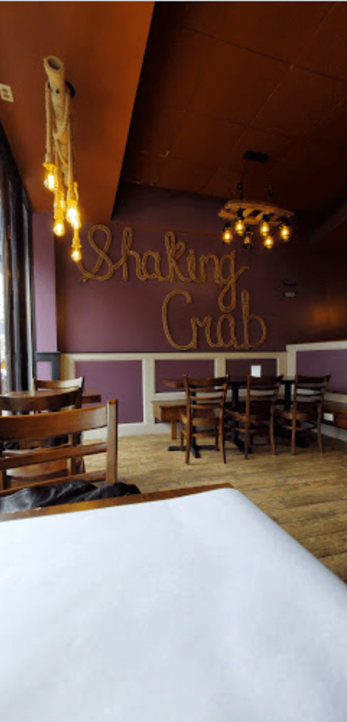 Interior of a restaurant with "Shaking Crab" sign made of rope, wooden tables, and warm lighting.