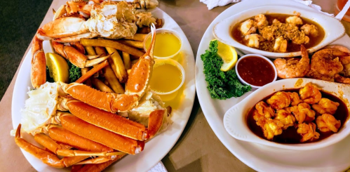 A platter of crab legs, fries, and shrimp with sauces and lemon wedges on a table.