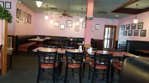 Interior of a restaurant with pink walls, empty tables, and framed pictures on the walls. Cozy and inviting atmosphere.