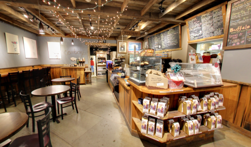 Cozy café interior with wooden beams, string lights, a counter displaying baked goods, and tables for seating.