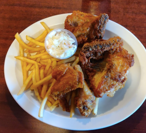 A plate of crispy fried chicken wings, golden French fries, and a small cup of coleslaw.