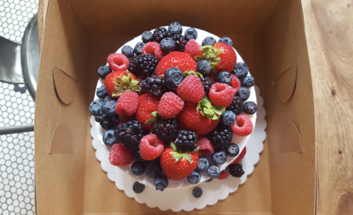 A round cake topped with an assortment of fresh strawberries, raspberries, blackberries, and blueberries in a box.