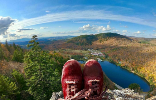 A pair of red sneakers on a rocky ledge overlooking a vibrant autumn landscape with mountains and a lake.