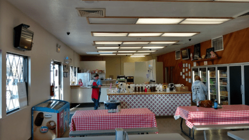 Interior of a casual eatery with checkered tablecloths, a service counter, and a variety of food and drink displays.