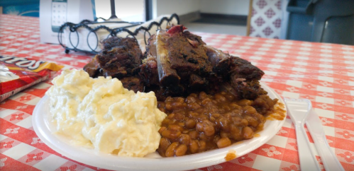 A plate with barbecue ribs, baked beans, and creamy potato salad on a checkered tablecloth.