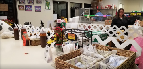 A cozy restaurant counter with baskets of utensils, condiments, and a woman carrying bags in the background.