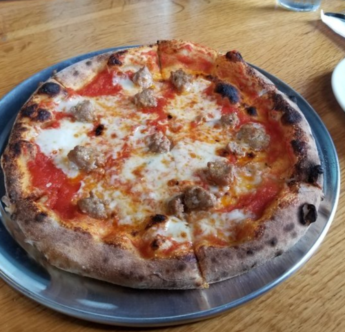 A freshly baked pizza on a metal tray, topped with cheese, tomato sauce, and small meatballs.