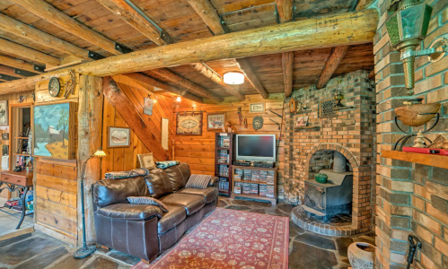 Cozy rustic living room with wooden beams, a leather couch, a TV, and a brick fireplace. Warm and inviting atmosphere.