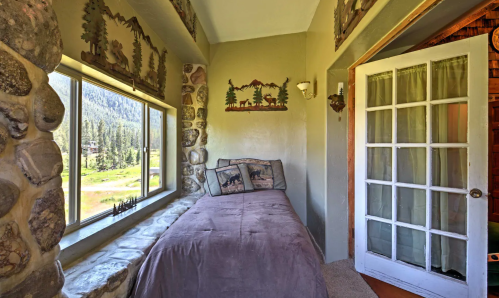 Cozy bedroom nook with stone walls, a single bed, and a large window overlooking a scenic mountain view.
