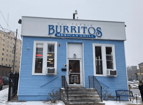 A blue building with a sign reading "California Burritos Mexican Grill," featuring an open sign and snowy surroundings.