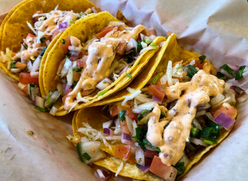 Three tacos filled with rice, diced tomatoes, onions, and drizzled with a creamy sauce, served in a basket.