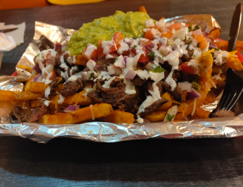 A plate of loaded fries topped with beef, guacamole, diced tomatoes, onions, and drizzled with sauce.