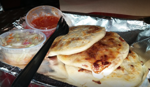 Three golden-brown pupusas on a tray, accompanied by salsa and coleslaw in small containers.