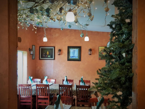 Cozy restaurant interior with orange walls, festive decor, a Christmas tree, and tables set for dining.