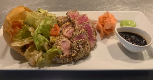 A plate featuring sesame-crusted tuna, salad, pickled ginger, wasabi, and a small bowl of soy sauce.