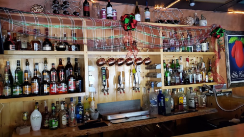 A wooden bar shelf filled with various bottles of liquor, beer taps, and festive decorations overhead.