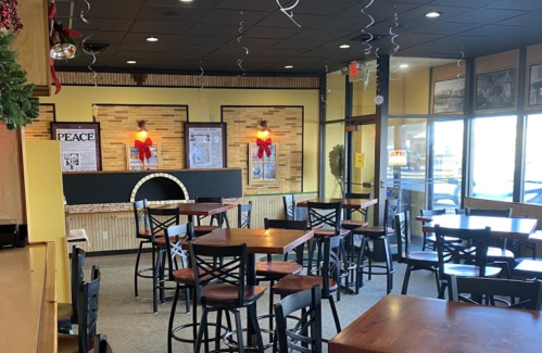 A cozy restaurant interior with wooden tables, high chairs, and festive decorations, featuring a fireplace and large windows.
