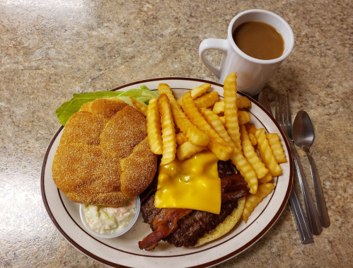 A plate with a cheeseburger, crinkle-cut fries, coleslaw, and a cup of coffee on a table.