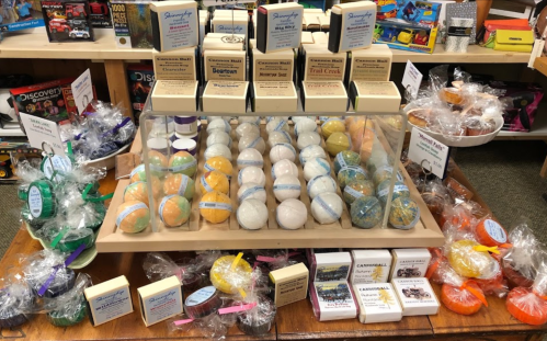 Display of colorful bath bombs and soaps arranged neatly on a wooden shelf in a store.