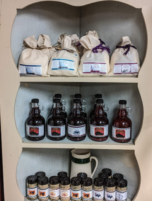 A wooden shelf displaying various jars and bags of homemade preserves and spices, neatly arranged.