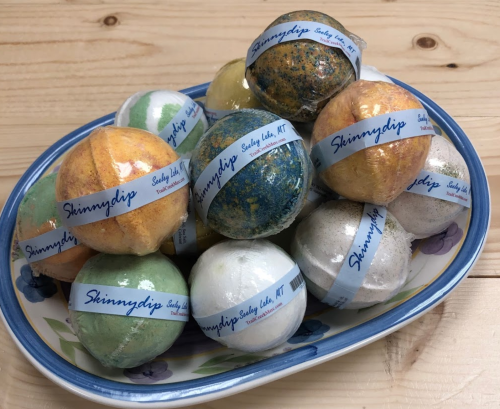 A colorful assortment of bath bombs arranged in a decorative bowl, featuring various textures and labels.
