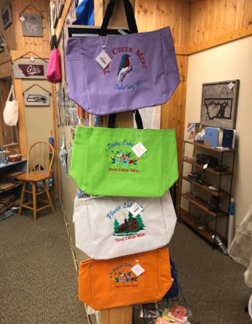 Four colorful tote bags hanging on a display, each with unique designs and tags, in a rustic shop setting.