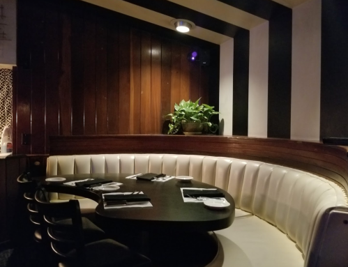 Cozy restaurant booth with a curved white leather seat, dark wooden walls, and a small plant on the table.