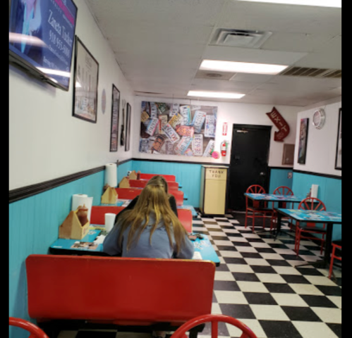A cozy diner with checkered floors, blue walls, and red seating. Two people sit at tables, enjoying their meals.