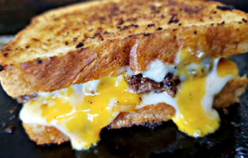 A close-up of a grilled sandwich with melted cheese, ground beef, and a runny egg, all between toasted bread.