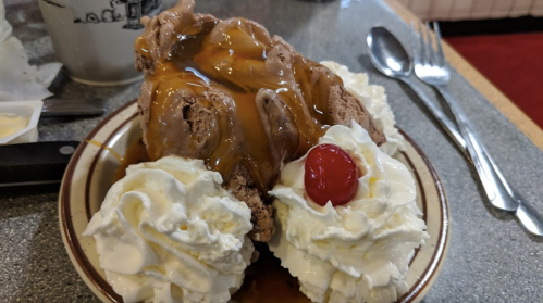 A dessert plate featuring chocolate ice cream topped with caramel sauce, whipped cream, and a cherry.