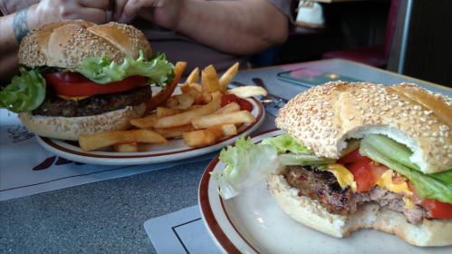 Two sesame seed burgers with lettuce, tomato, and cheese, served with a side of golden French fries on a table.