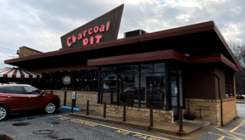 Exterior of Charcoal Dit restaurant with a red car parked outside and cloudy skies above.