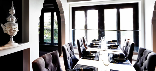 Elegant dining room with a long table set for a meal, featuring plush chairs and large windows letting in natural light.