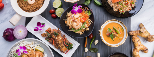 A vibrant spread of various Asian dishes, including noodles, seafood, curry, and garnished with fresh herbs and flowers.