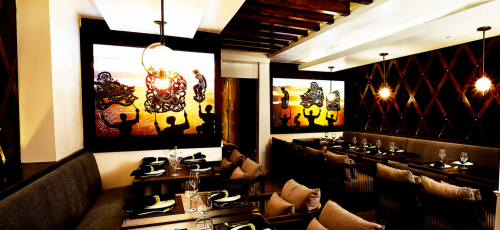 Elegant restaurant interior featuring wooden beams, plush seating, and vibrant wall art. Tables set for dining.