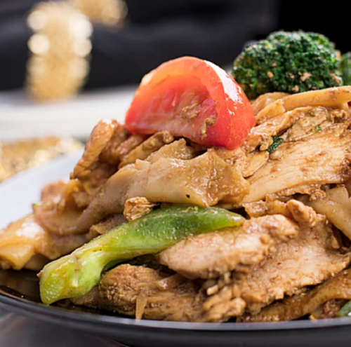 A plate of stir-fried chicken with vegetables, including broccoli, green pepper, and tomato slices.