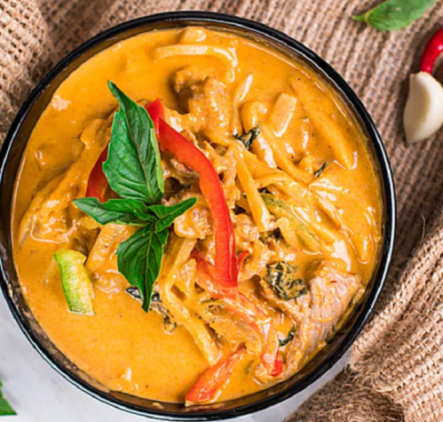A bowl of creamy curry with vegetables and herbs, garnished with fresh basil and red pepper strips.