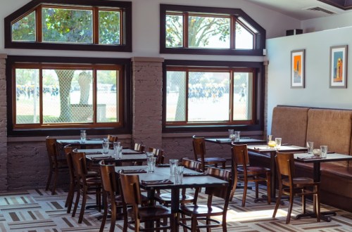 Cozy restaurant interior with wooden tables and chairs, large windows, and a view of an outdoor area.