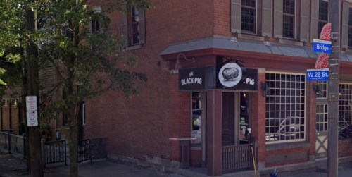 Exterior view of a brick building featuring a sign for "The Black Pig" restaurant at the corner of W. 28th St. and Bridge.