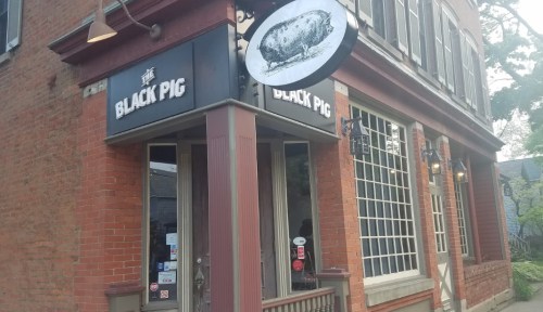 Exterior of a restaurant named "Black Pig," featuring a sign with a pig illustration and brick architecture.